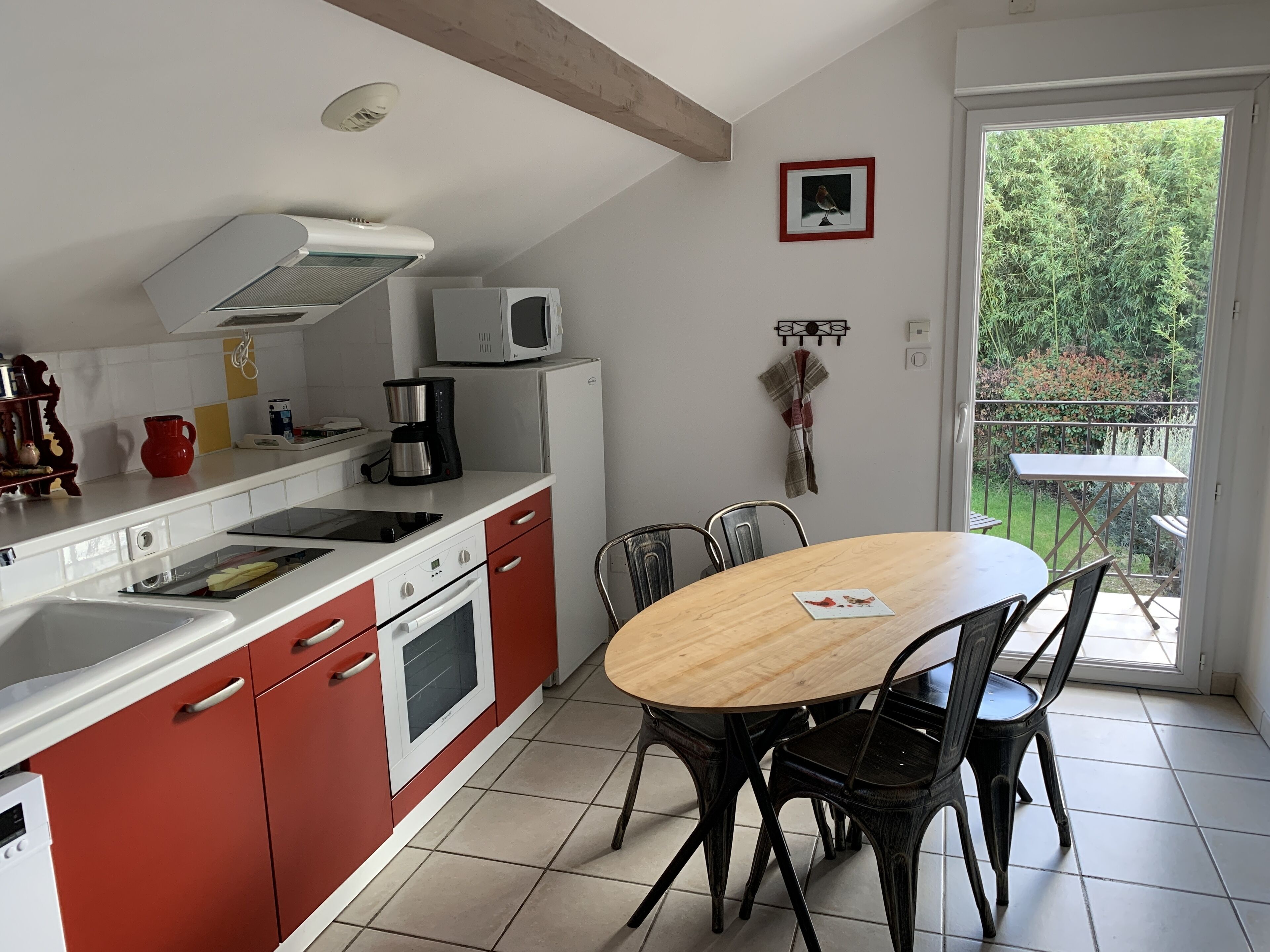 Una cocina con comedor, armarios blancos, microondas, cafetera y vista a zonas verdes.
