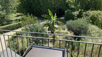 A balcony with a metal railing, a cushioned seat, and a view of a garden with various plants and a banana tree.
