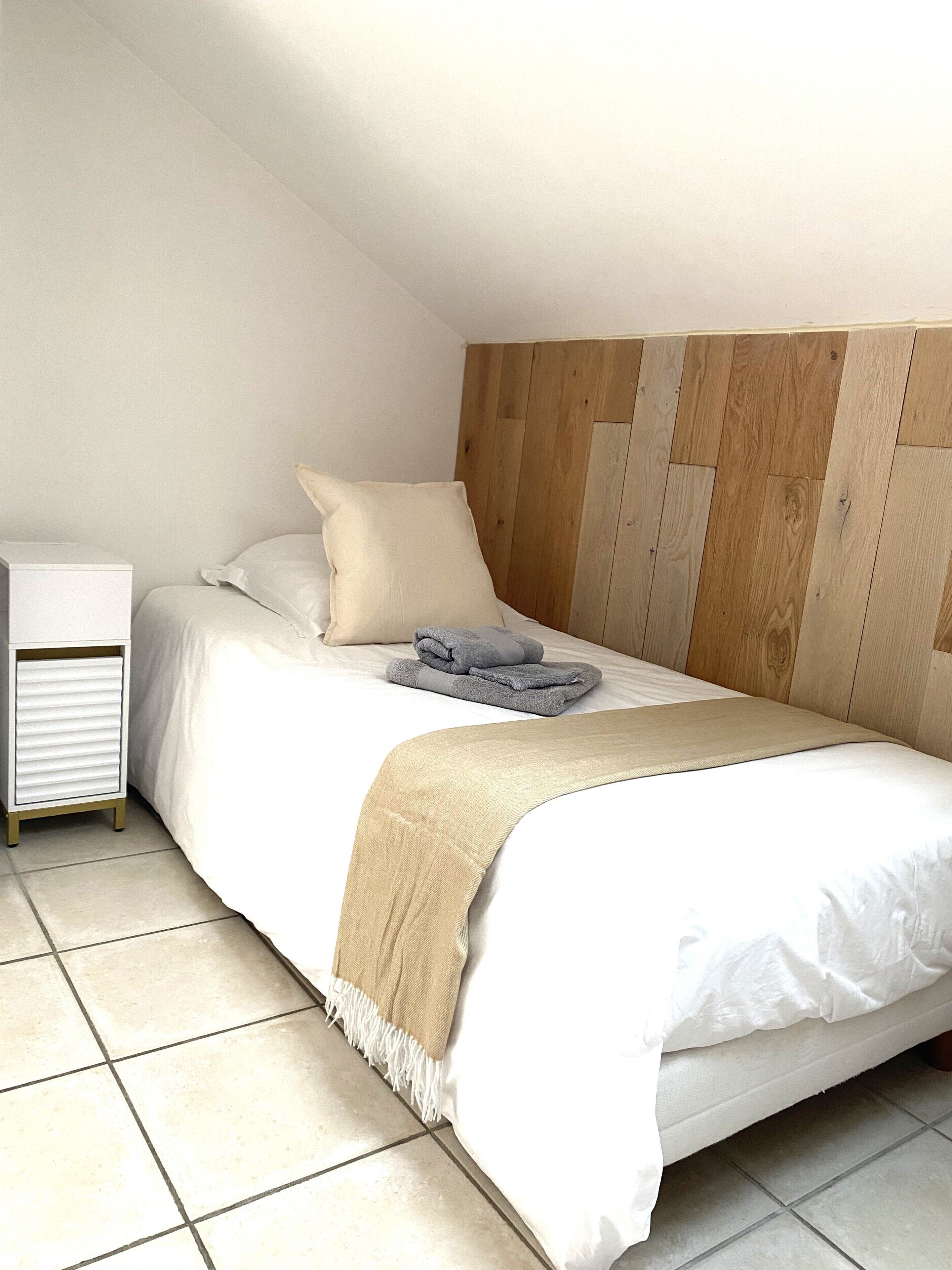 Een slaapkamer met een bed, kussens, een deken, een nachtkastje en een houten hoofdbord.