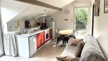 A modern kitchen with red and white cabinetry, a dining area with a wooden table and chairs, and a living room with a sofa and a large window.
