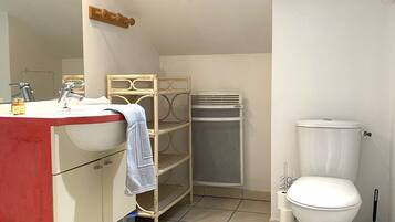 Een badkamer met een wit wastafel, spiegel en toilet. Er is een plankje met een handdoek en een toiletborstel.
