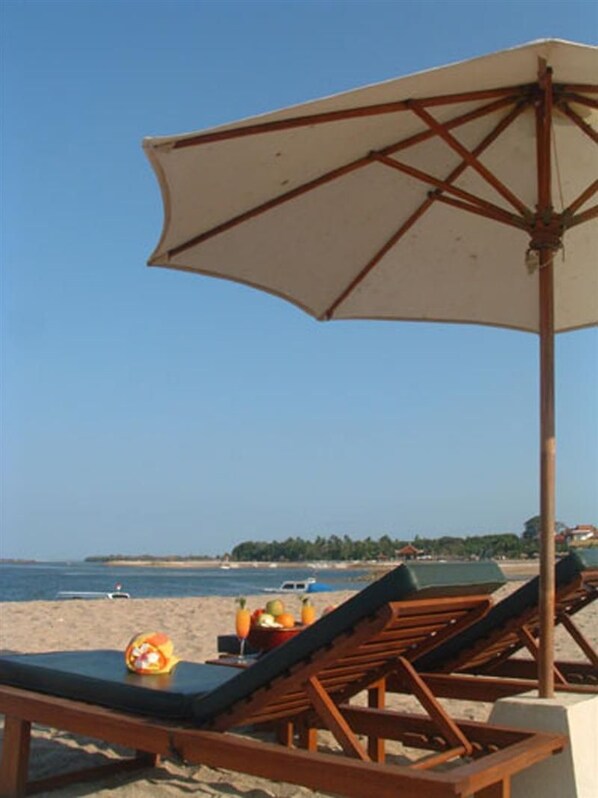 Escena costera con sillones de playa y una sombrilla, cielo despejado y una línea de costa distante.