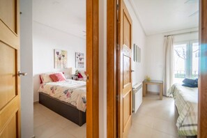 Une chambre à coucher comprenant un lit, une table de chevet, une fenêtre avec des rideaux et une porte donnant sur une autre pièce.