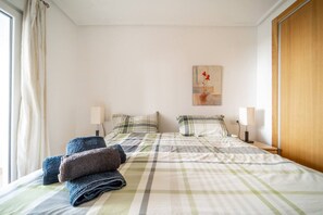 Een hotelkamer met een bed, twee nachtlampjes, een raam met gordijnen en een schilderij aan de muur.