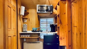 Une cuisine compacte dotée de meubles en bois, d’un four à micro-ondes, d’un petit réfrigérateur et d’une fenêtre laissant entrer la lumière naturelle.