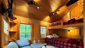 L’intérieur d’une cabine, avec un canapé, un lit recouvert d’une couverture à carreaux, une petite table sur laquelle se trouvent une tasse et une pâtisserie, et un panneau indiquant qu’il s’agit d’une cabine.