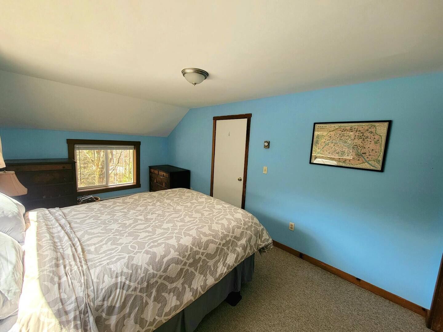 Ein Schlafzimmer mit Bett, Kommode, Fenster und Tür, sowie einer Karte an der Wand.