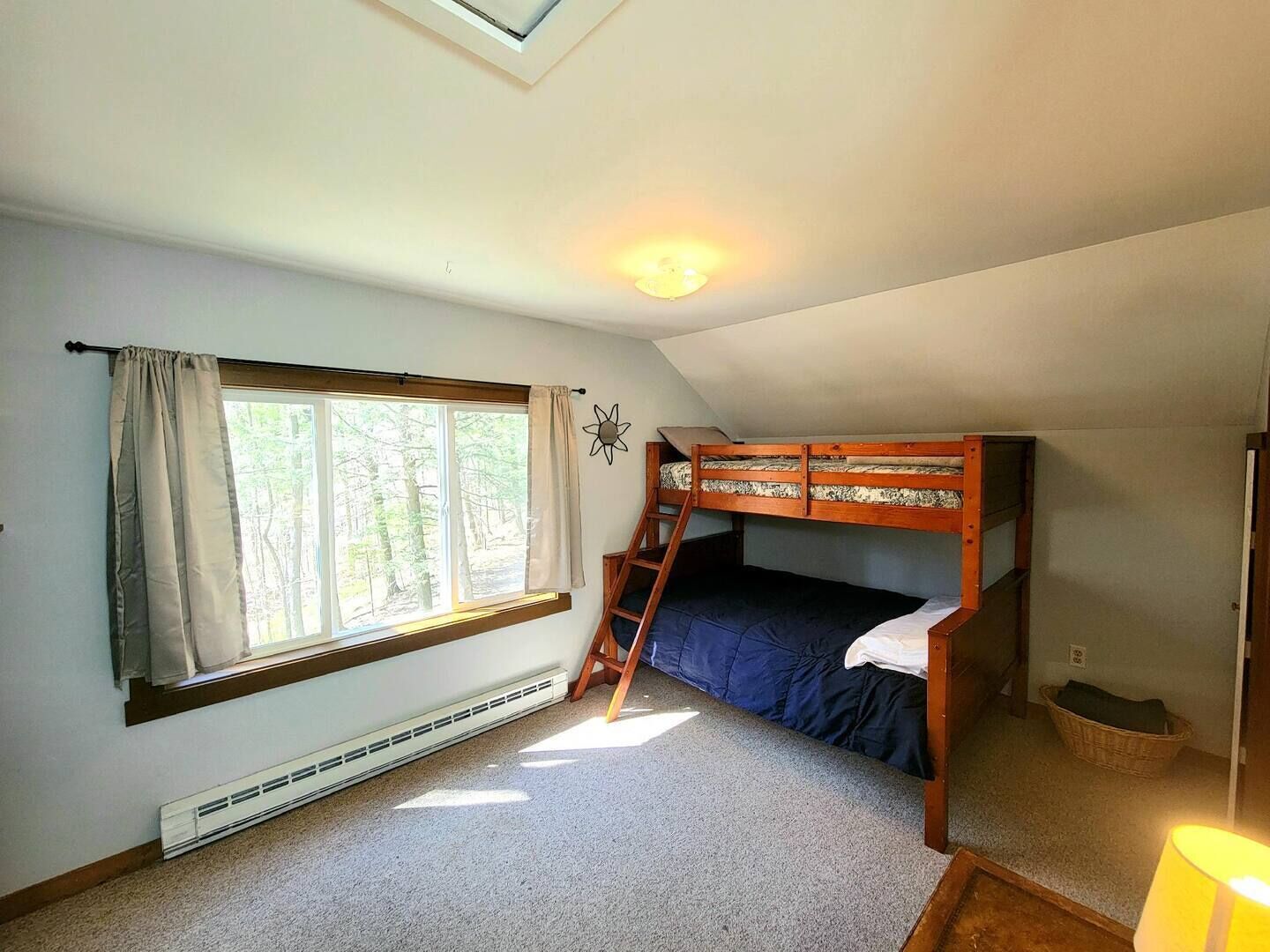 A small, cozy room with a bunk bed, a window with curtains, a skylight, and a heater.