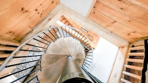 Un escalier en colimaçon dans un intérieur en bois, avec des poutres apparentes et une vue dégagée sur le plafond.