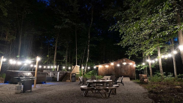 An outdoor patio area with wooden tables and benches, a barbecue grill, and a wooden shelter.