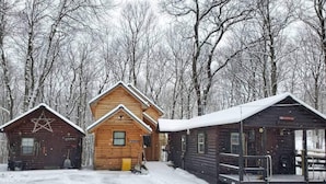 A cabin complex with multiple wooden buildings, including a central lodge and smaller cabins, surrounded by a snowy forest.