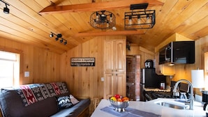 A cozy cabin interior with a wooden interior, a kitchenette, a dining area with a bench, and a sign on the wall.