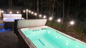 An outdoor hot tub with a wooden deck and string lights, surrounded by trees.