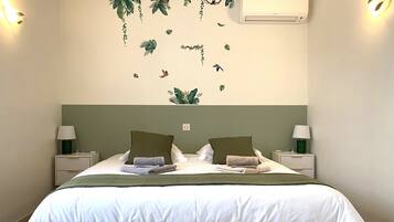 Een net opgemaakt bed met kussens en dekbed, twee nachtkastjes met lampen, en een wandairconditioner.