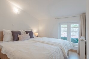 A bedroom with a large bed, a nightstand, a window with curtains, and a view of the outside. - Luxury Mountain Villa W.heated Pool & Largegarden (Muc)