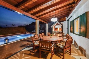 An outdoor patio with a pool, wooden furniture, and a stone wall. - Luxury Mountain Villa W.heated Pool & Largegarden (Muc)