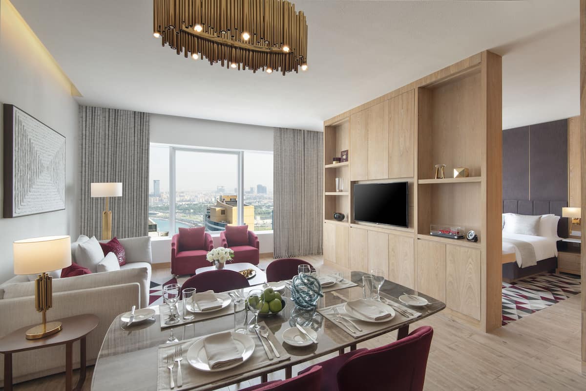 Una habitación de hotel moderna con comedor, televisor y vistas a la ciudad.