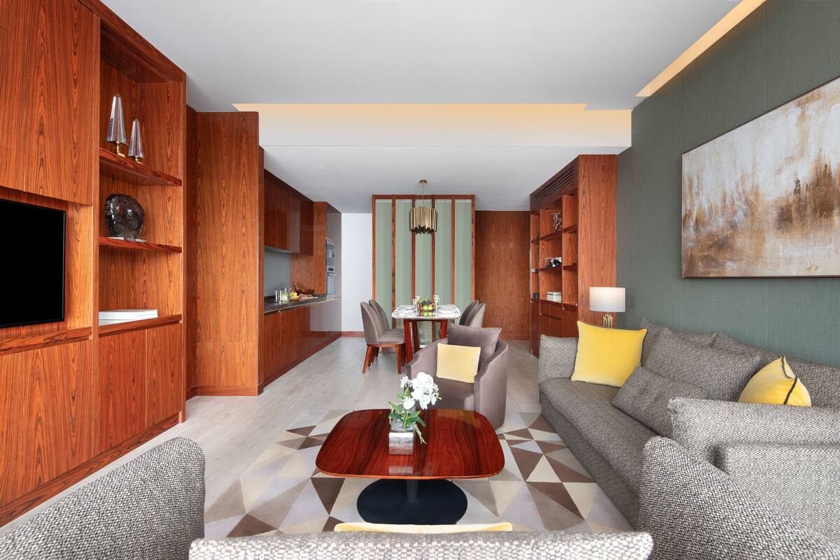 Una sala de estar moderna con un mueble de madera, un sofá gris con almohadones amarillos, una mesa de comedor con sillas y un cuadro abstracto grande en la pared.