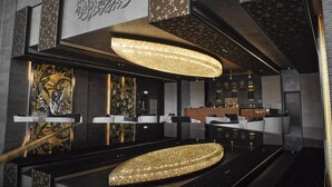A modern hotel lobby with a reception desk, seating area, and decorative wall panels. - The Bentley Luxury Hotel and Suites (Doha)