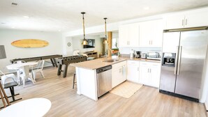 Une cuisine moderne dotée d’un îlot central, d’appareils électroménagers en acier inoxydable et d’un coin repas avec des chaises blanches.