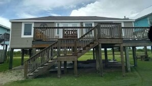 A two-story house with a wooden deck and a staircase leading to the upper level. - Beach and river view cottage with deck and specatuclar views. (Matagorda)