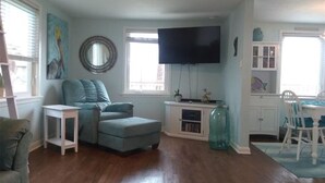A living room with a teal sofa, a flat-screen TV, a small table, and a fish-themed decoration. - Beach and river view cottage with deck and specatuclar views. (Matagorda)
