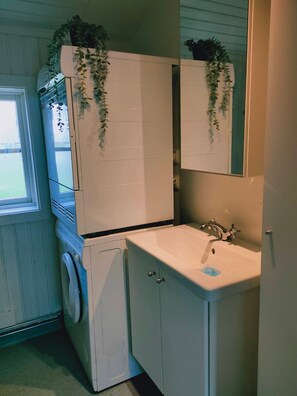 Ein kleines Badezimmer mit Waschmaschine, Waschbecken und Spiegel.