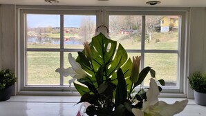 A room with a large window, a potted plant, and a view of a lake and houses. - Charming 2-bed House at the Lake Close Gustavsfors (Gustavsfors)