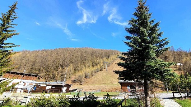 A lodge with a mountain backdrop, a clear sky, and a forested hill. - Maison des skieur- ski out (Sestriere)