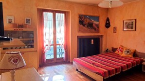 A bedroom with a bed, a desk, a chair, a wardrobe, and a window with curtains. - Maison des skieur- ski out (Sestriere)