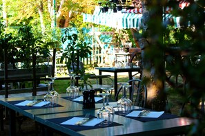 A dining table set outdoors with multiple chairs, a potted plant, and a view of a park with a fence and trees. - Le Fruit Défendu (Rueil-Malmaison)