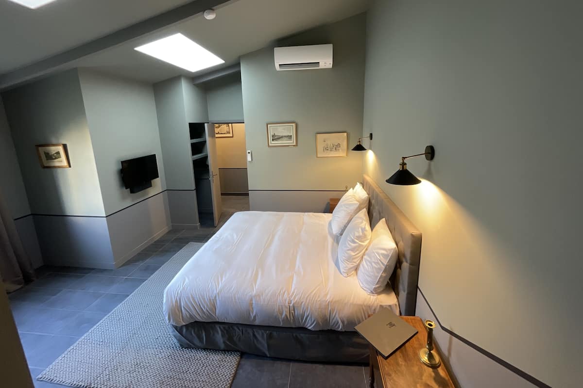 A bedroom with a bed, a desk, a chair, a TV, and a window.