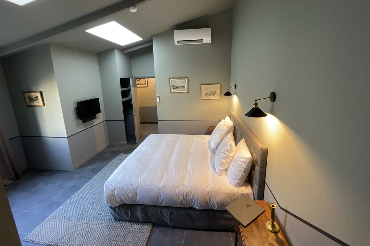 A bedroom with a bed, bedside table, lamp, and a TV on the wall.