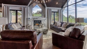 A spacious living room with a fireplace, leather sofas, and large windows offering a view of the outdoors.