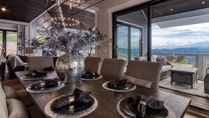 A dining area with a large table set for six, surrounded by comfortable seating. A large vase with flowers is placed in the center.