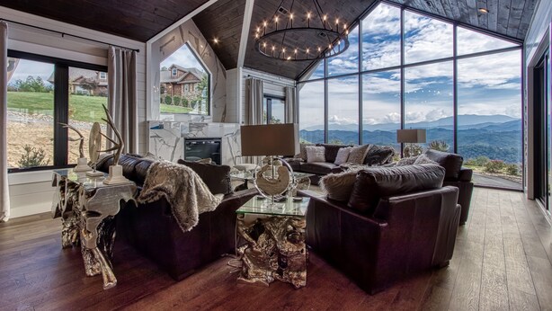 A spacious living room with a large window offering a mountain view, a modern chandelier, and a unique wooden ceiling.