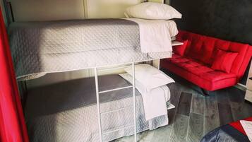 A bunk bed with a mattress and pillows, a red sofa, and a tiled floor.