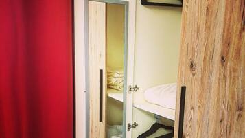 Une armoire avec un miroir, une tringle à vêtements et un lit avec une couette blanche.