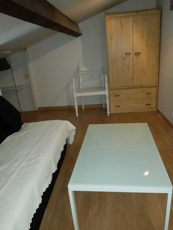 Ett sovrum med en säng, ett vitt bord, en trägarderob och en stol.