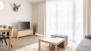 Un soggiorno moderno con un tavolino in legno, un divano grigio, una TV a schermo piatto su un supporto in legno, un tavolo da pranzo con sedie e un cervo appeso al muro.