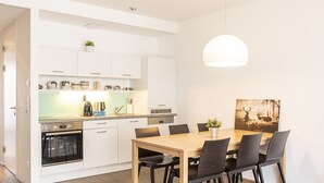 Una cucina moderna con mobili bianchi, forno integrato e zona pranzo con tavolo e sedie in legno.