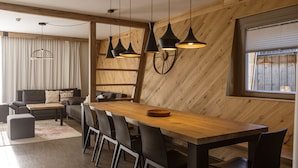 Un comedor moderno con una mesa de madera y sillas negras, una pared de madera con un reloj, y una ventana con persianas.