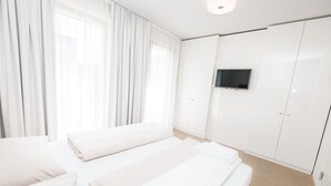 Una habitación de hotel moderna con dos camas, un televisor de pantalla plana y un gran ventanal con cortinas traslúcidas.