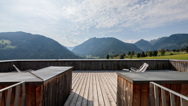 Una terraza de madera con dos sillones y vistas a montañas.