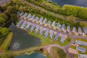 An aerial view of a caravan park with rows of caravans, a body of water, and a road.