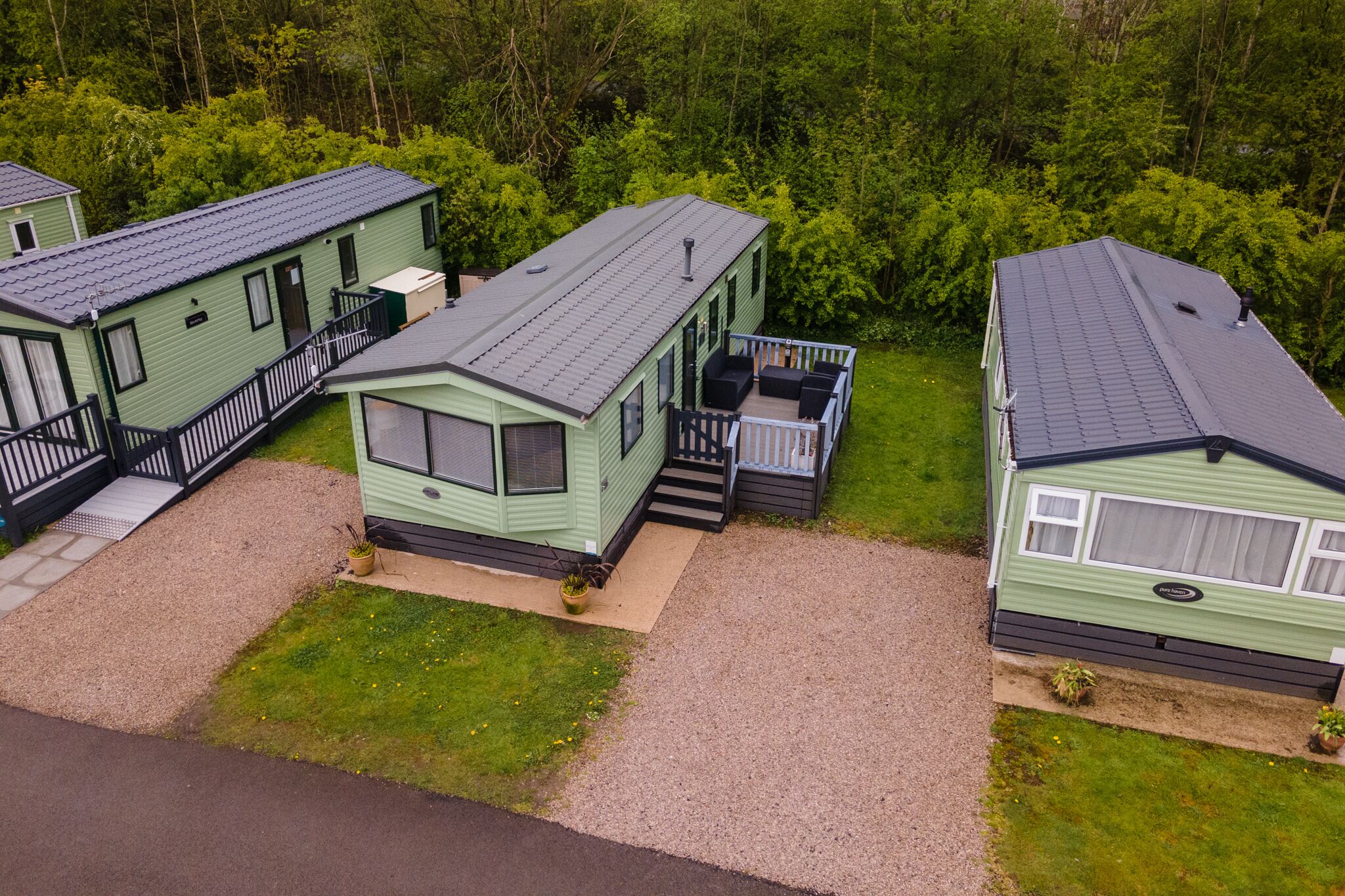 A row of green mobile homes with attached porches and a gravel driveway.
