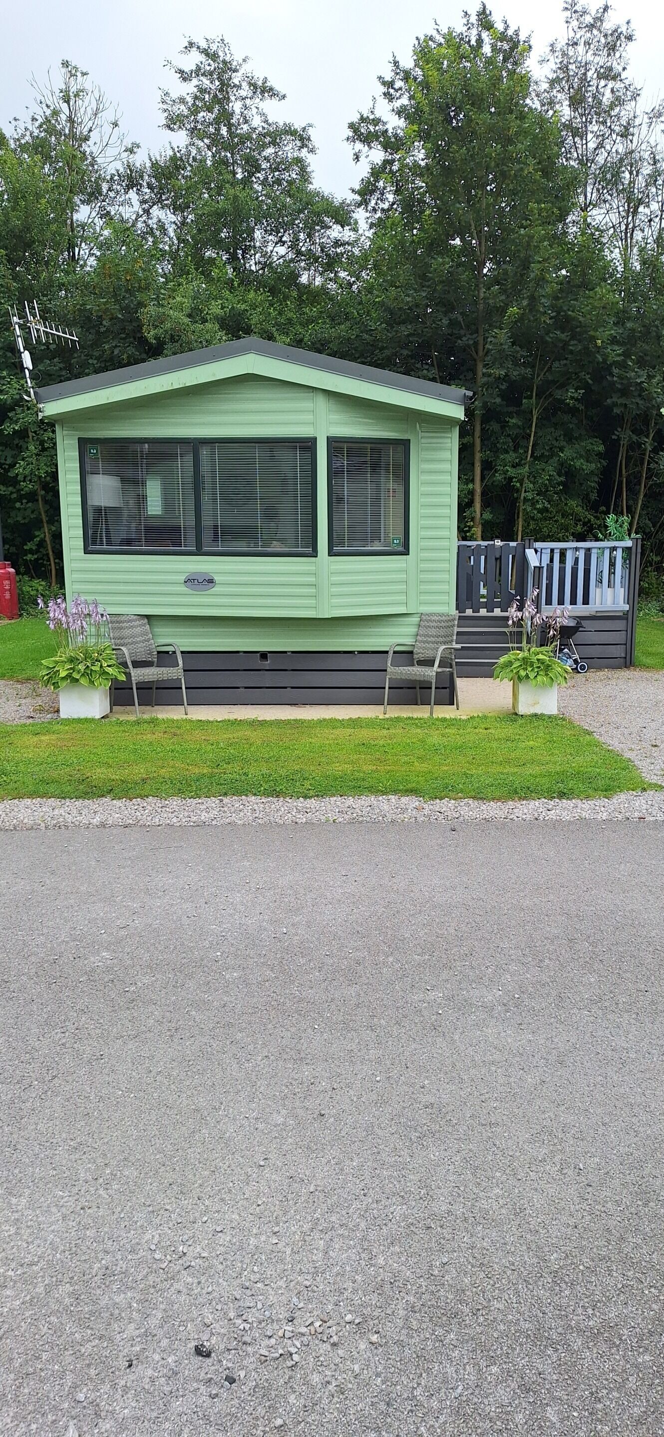A green mobile home with a porch, two potted plants, and a small deck.