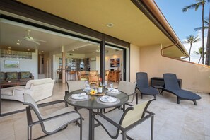 A sunlit patio with a round table set for dining, surrounded by lounge chairs and a modern kitchen in the background.