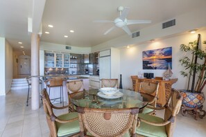 A modern kitchen with a glass dining table, wicker chairs, and a ceiling fan.
