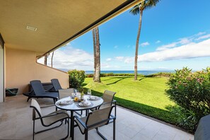 An outdoor patio with a table set for dining, overlooking a well-manicured lawn and a view of the ocean.